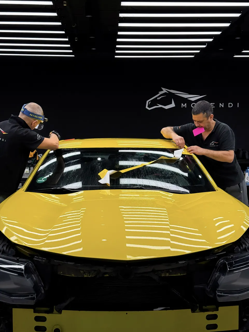 Два мастера оклеивают капот жёлтого Chevrolet Camaro плёнкой